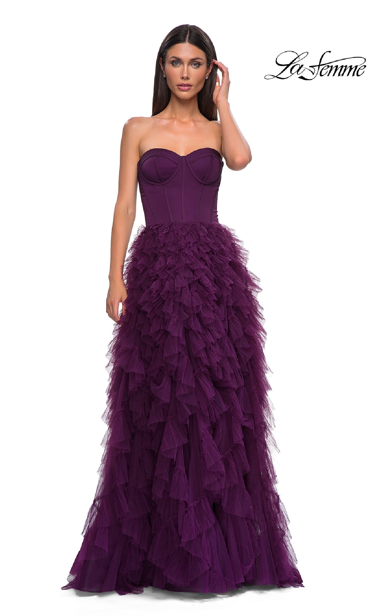 A woman stands against a white background wearing the Strapless Long Ruffled Prom Dress: La Femme 32760, featuring a corset-style bodice and layered tulle skirt.